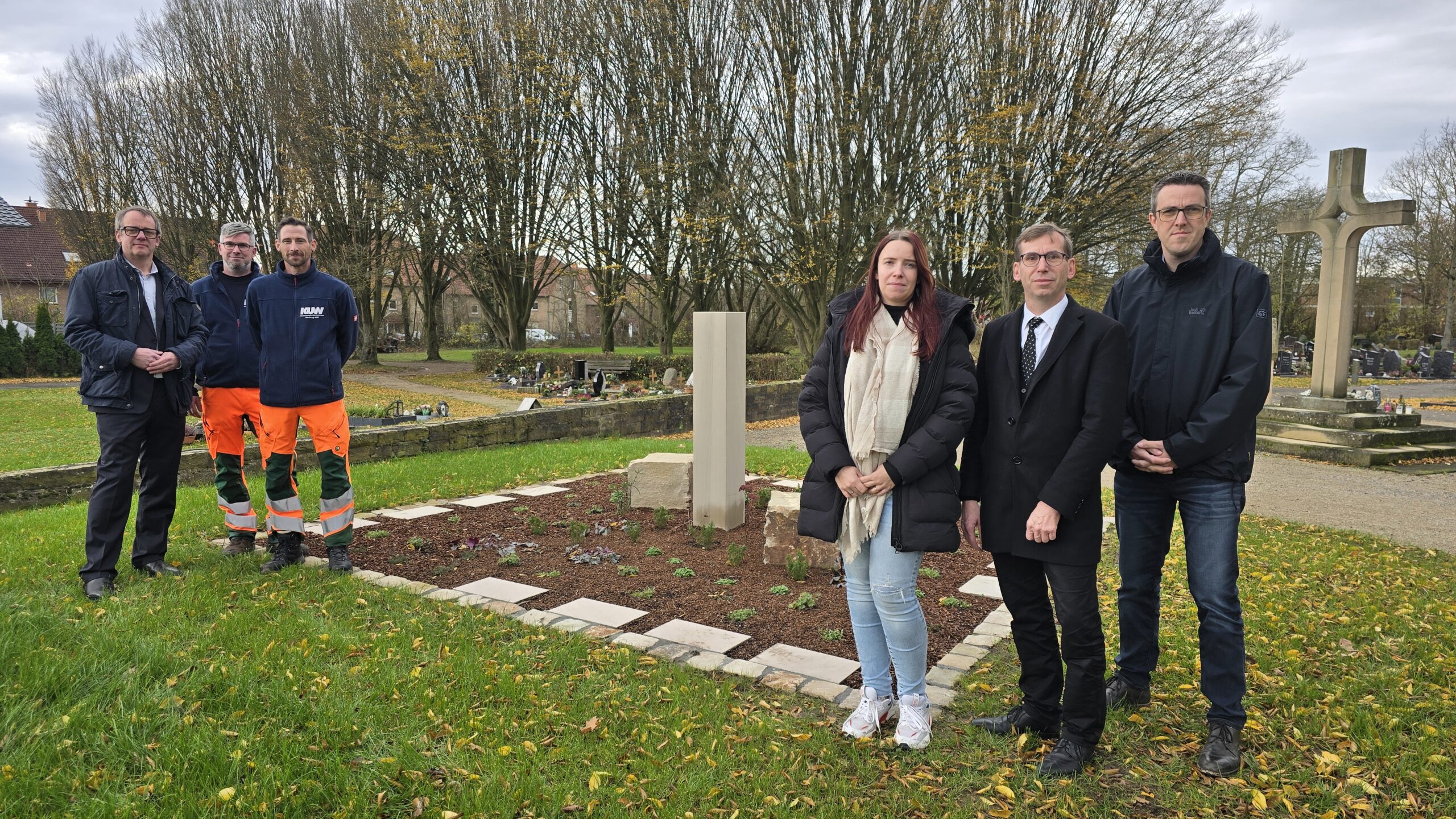 Von links: Leander Sasse, Geschäftsführer des Kommunalunternehmens Warburg, Thomas Deist und Bernd Berlage (beide KUW), Denise Flinkmann (KUW – Friedhofsverwaltung), Bürgermeister Tobias Scherf und der erste Beigeordnete Andreas Niggemeyer vor einer großen Urnengemeinschaftsgrabanlage auf dem Warburger Stiepenfriedhof. © Hansestadt Warburg